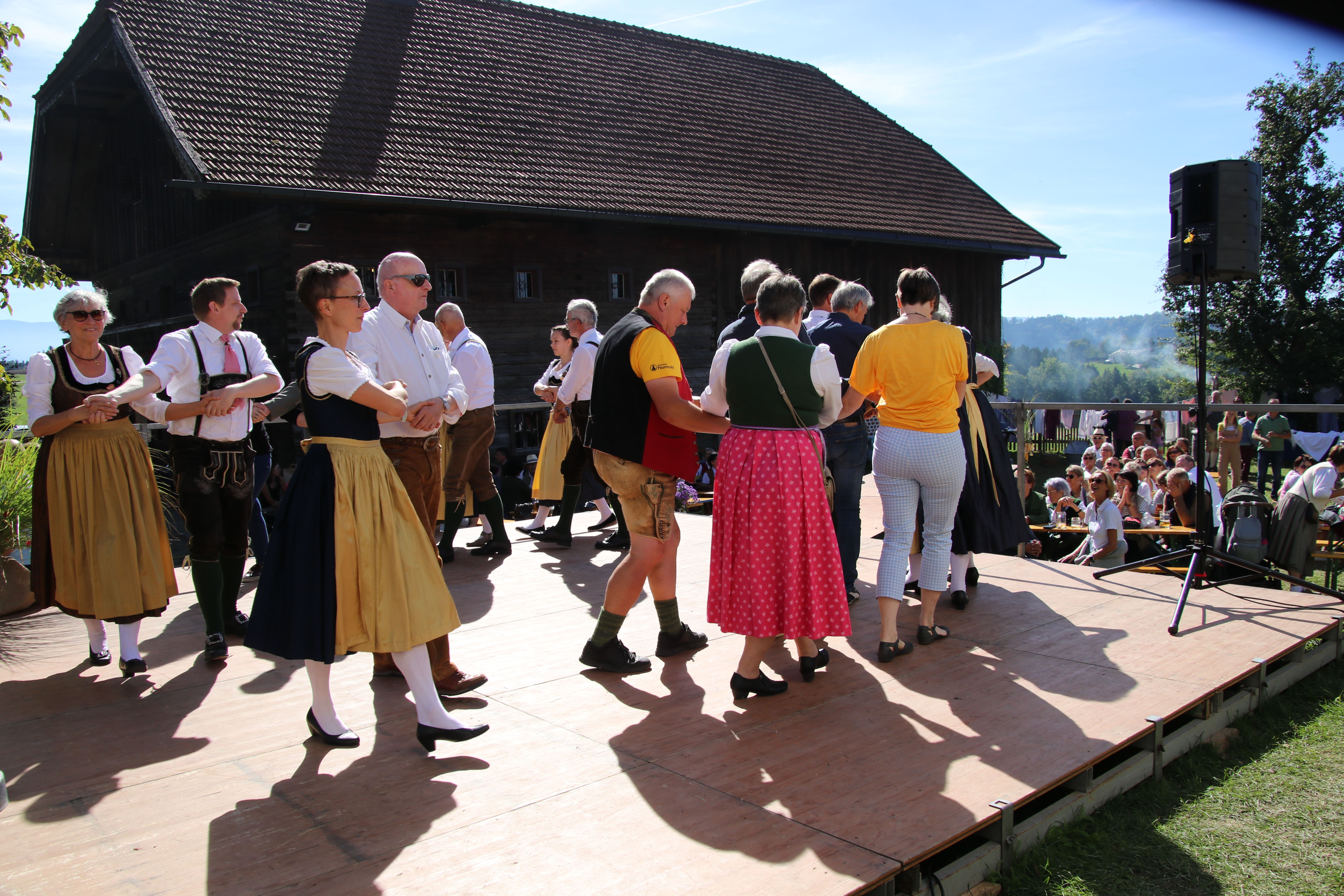 Trachtengruppe tanzt auf einer Bühne vor einem Holzhaus in Österreich
